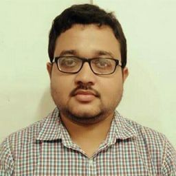 Person wearing a checkered shirt, standing against a plain light-colored background.