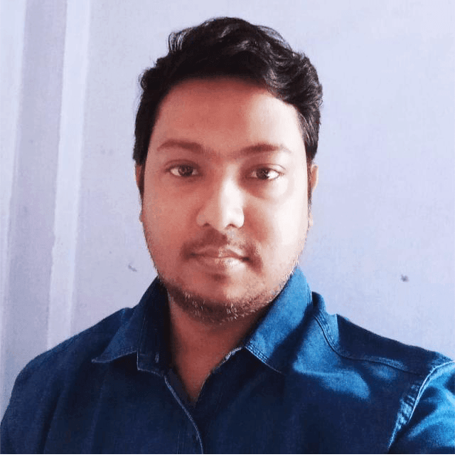 Person wearing a blue denim shirt standing against a light-colored wall.