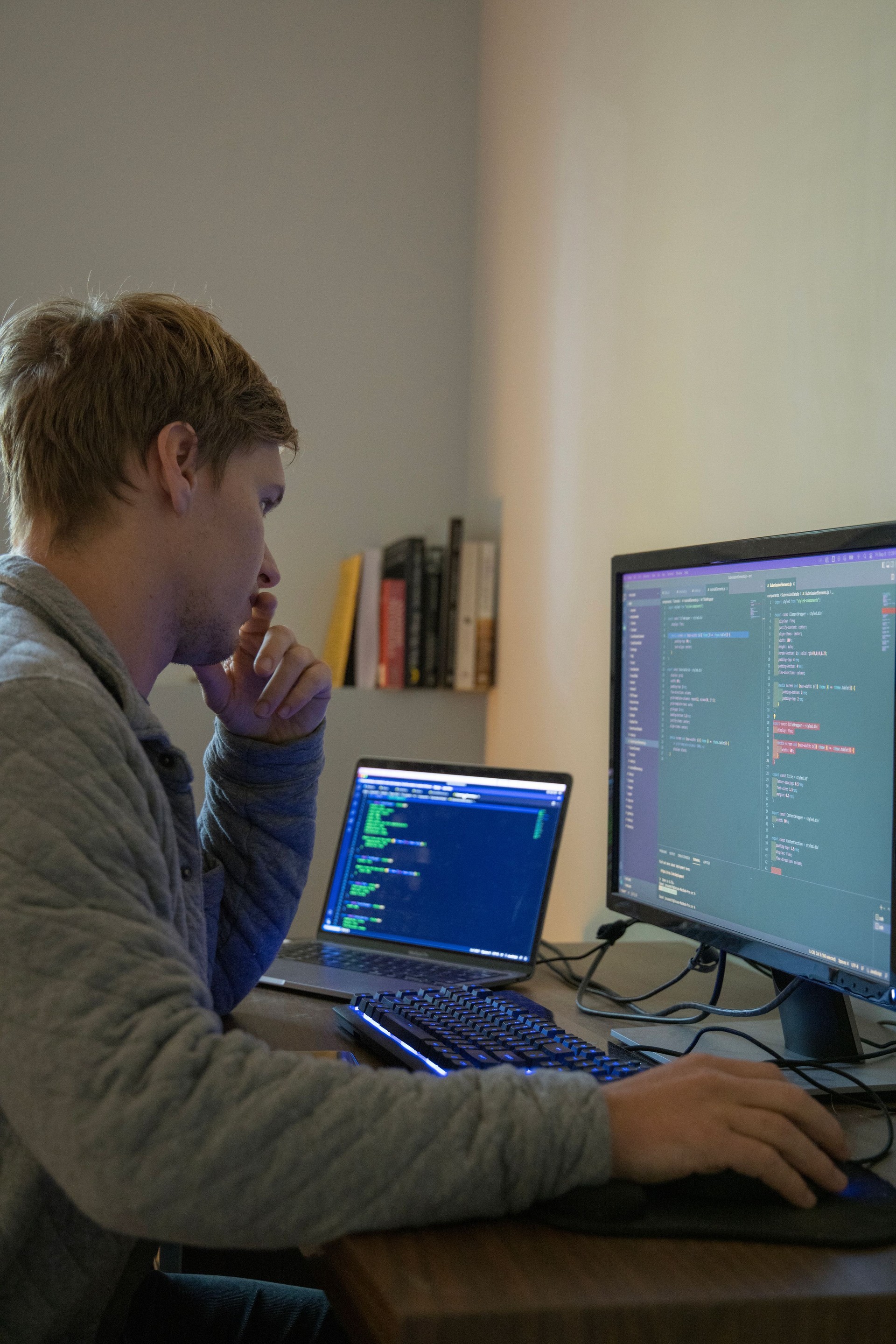Young man uses multiple computers while coding, developing web site